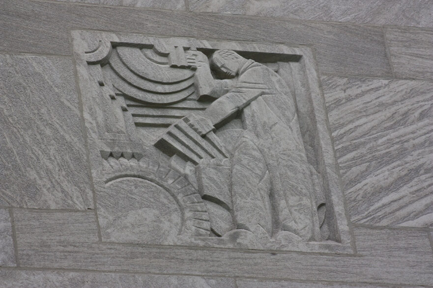 33 Carving on the upper area of the north and south extensions of City Hall, this is an Art Deco figure operating machinery, circa 2022.