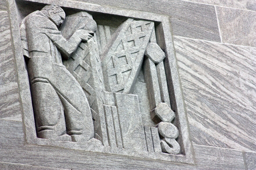 35 Carving on the upper area of the north and south extensions of City Hall, this is an Art Deco figure operating a crane type of machine, circa 2022.