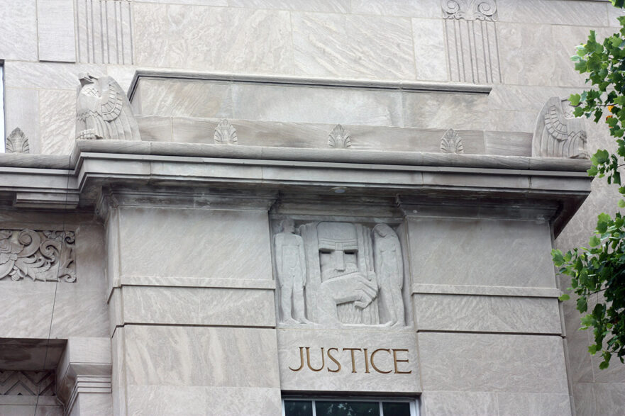 36 West façade, south corner, note the Art Deco carving of Justice, as well as the eagles and leaf that adorn the banding around the top of the building, circa 2022.